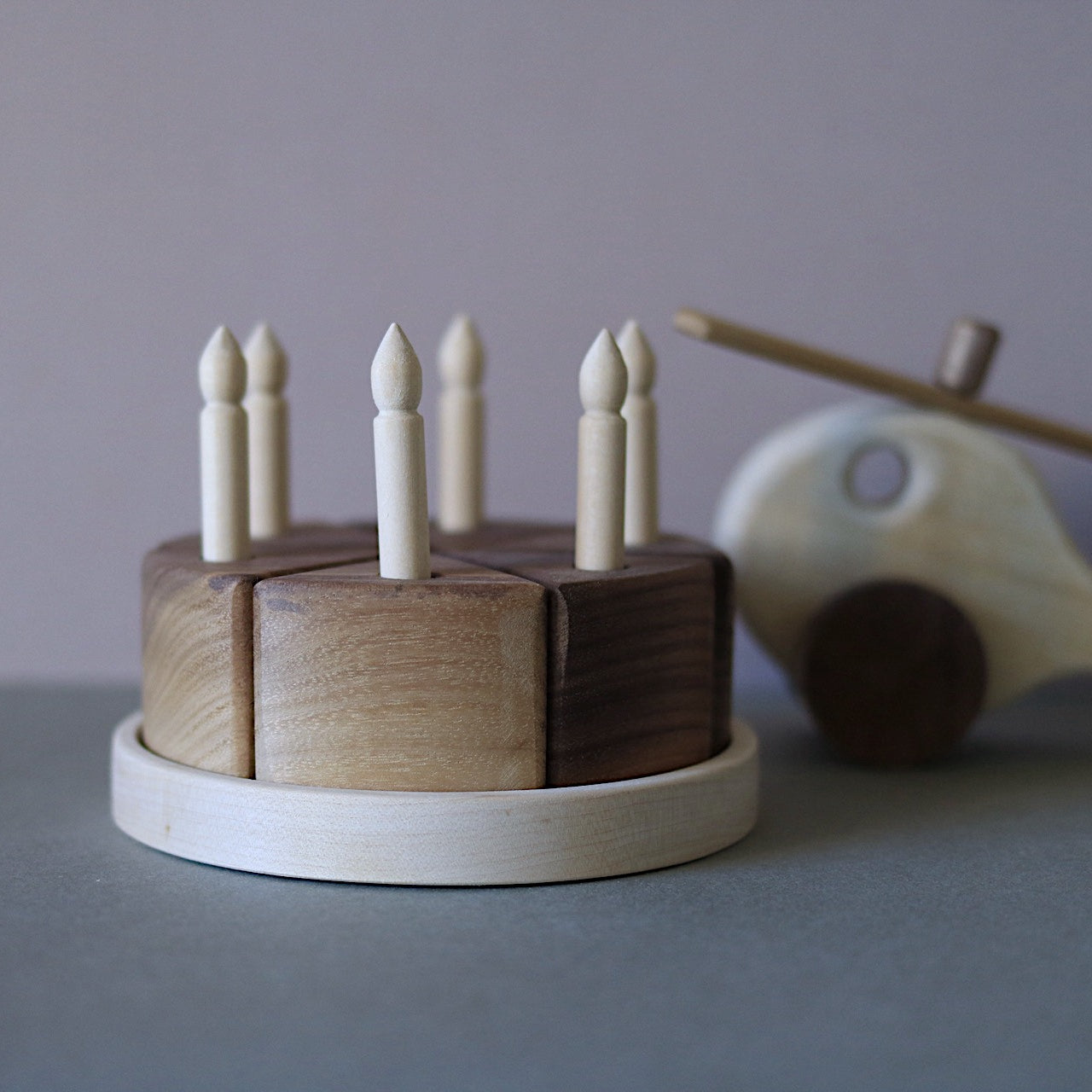 Wooden toy cake with candles and a wooden helicopter on a gray surface