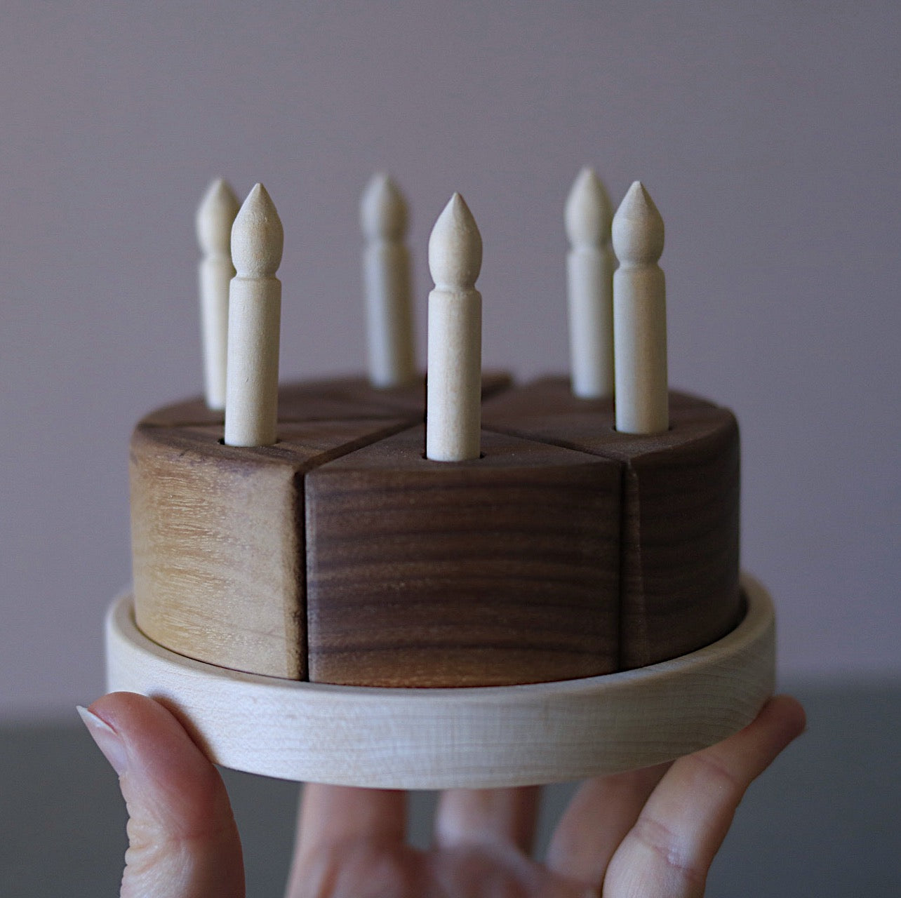 Wooden toy cake with candles held by a hand against a plain background