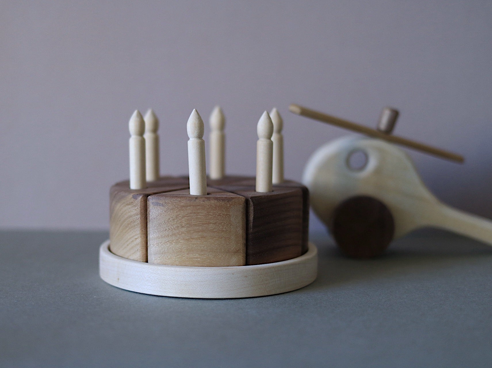 Wooden toy cake with candles and a wooden helicopter on a gray surface