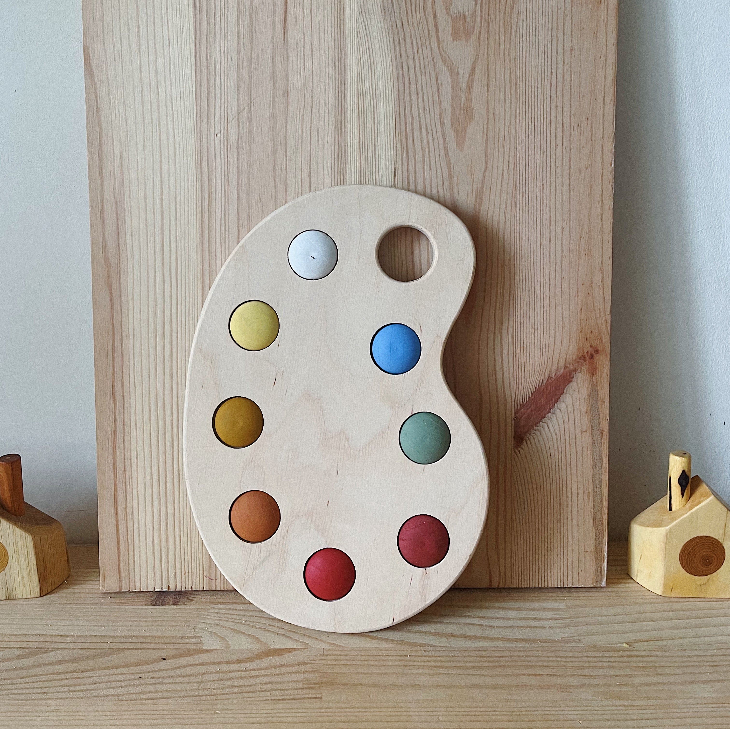 A wooden artist's color palette toy with hand-painted colors in various sections, displayed against a wooden background.